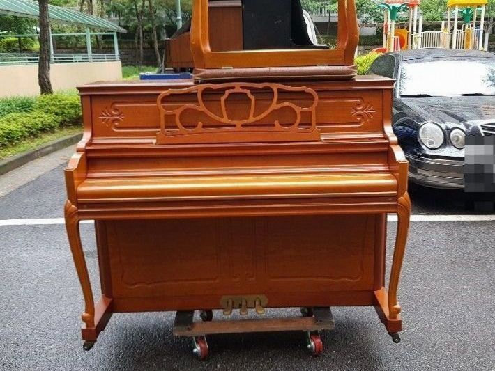 주차장에서 의자를 올린 채 차량을 기다리는 원목 업라이트 피아노