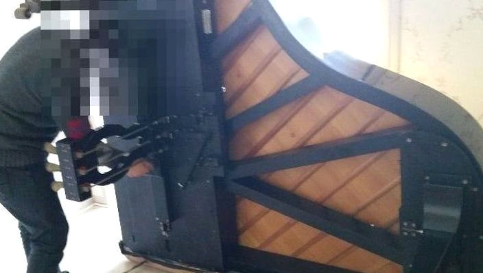 옆으로 세운 그랜드피아노에서 부품을 분리하는 작업자
