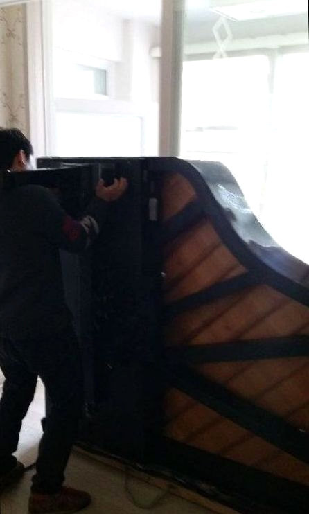 다리를 떼고 옆으로 세운 그랜드피아노를 붙잡은 작업자