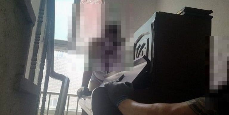 좁은 계단참에서 업라이트 피아노를 붙잡고 내리는 작업자들